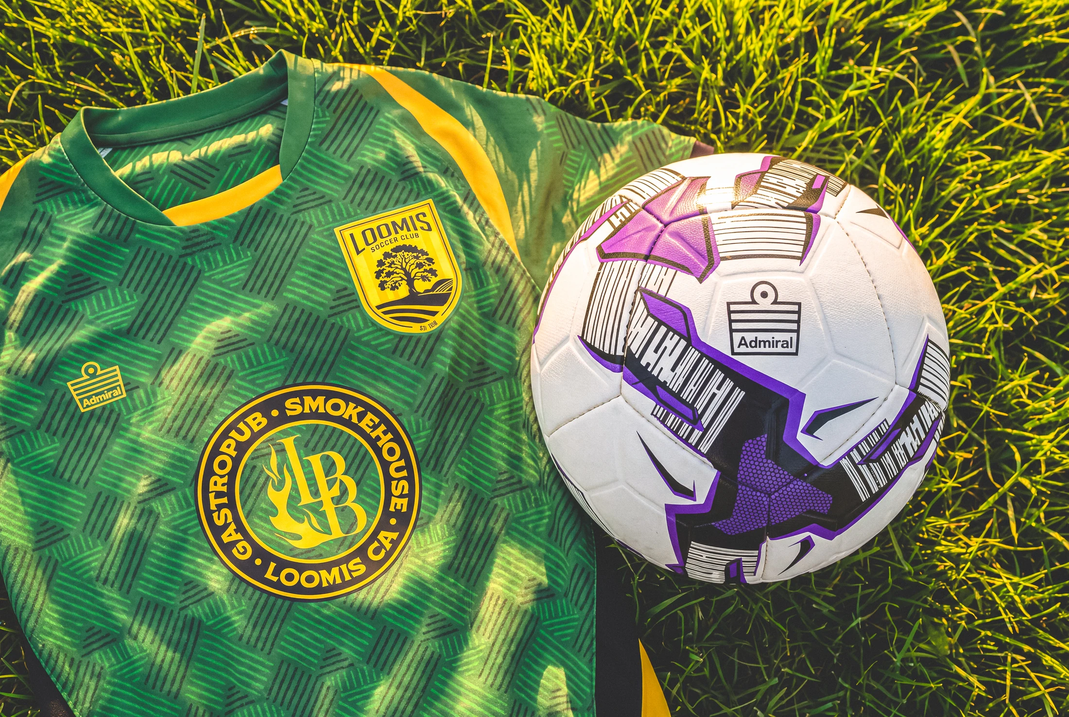 Green Loomis alternate shirt and ball arranged in grass